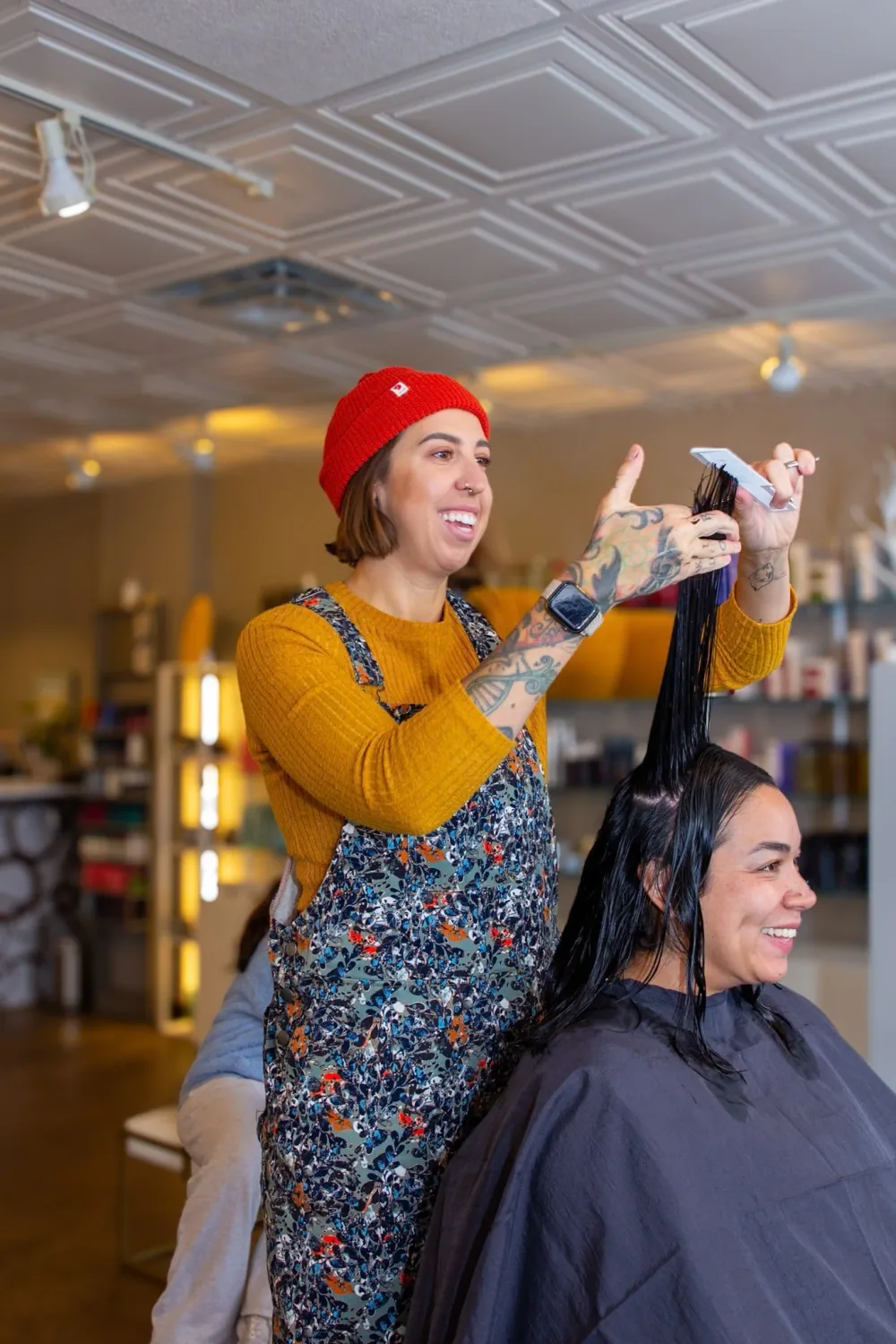 A Starling Salon stylist in a red beanie smiling while cutting a client's hair